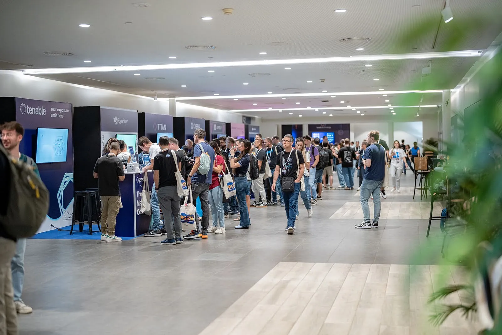 Wide view of the expo floor lined with sponsor booths and attendees carrying tote bags